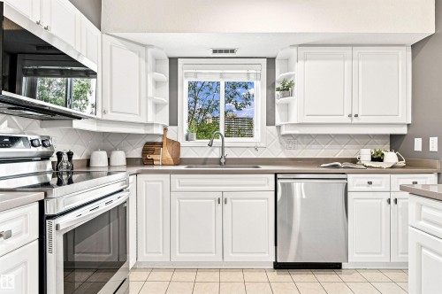 White cabinetry, stainless steel appliances, tile flooring, window over sink, and a decorative tile backsplash - #432 6703 172 St Nw, Edmonton, AB 