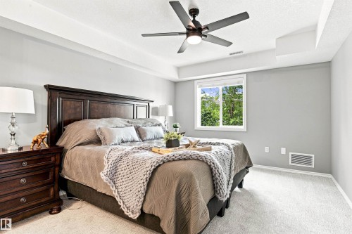 Recessed ceiling, ceiling fan with integrated lighting, wood-finish headboard, window with exterior scenery, and carpeted flooring - #432 6703 172 St Nw, Edmonton, AB 