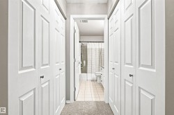 Hallway featuring bi-fold closet doors with dark hardware, leading to a bathroom with a ceramic tile floor, bathtub, and toilet - 