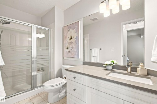 Glass-enclosed shower with frosted bands, white vanity with paneled doors and drawers, gray countertop, undermount sink, and polished chrome faucet - #432 6703 172 St Nw, Edmonton, AB 