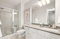 Glass-enclosed shower with frosted bands, white vanity with paneled doors and drawers, gray countertop, undermount sink, and polished chrome faucet - 