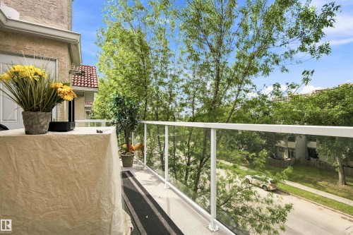 Balcony with glass panel railings, textured stucco exterior, and a white exterior door - #432 6703 172 St Nw, Edmonton, AB 