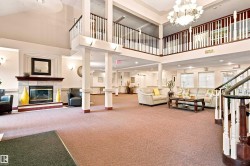Spacious two-story lobby featuring a tiled fireplace, an elegant chandelier, and a grand staircase with white balusters and wood handrails - 