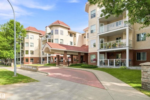 Multi-story building featuring a covered entrance, red tile roofing, multiple balconies with glass railings, and a stone-clad sign monument - #432 6703 172 St Nw, Edmonton, AB 