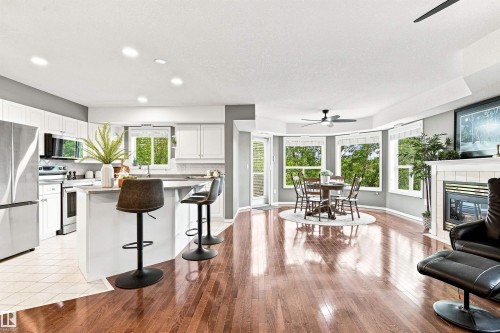 Hardwood flooring throughout, white kitchen cabinetry, stainless steel appliances, breakfast bar, and a fireplace with a white mantel - #432 6703 172 St Nw, Edmonton, AB 