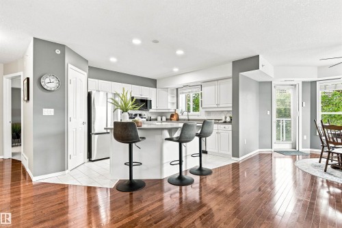 Kitchen featuring white cabinetry, stainless steel appliances, a center island with seating, and tile flooring - #432 6703 172 St Nw, Edmonton, AB 