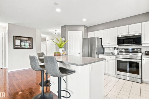 Kitchen featuring white cabinetry, stainless steel appliances, a center island with countertop seating, and tile flooring - #432 6703 172 St Nw, Edmonton, AB 