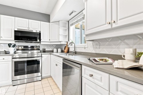 White cabinetry with brushed nickel hardware, stainless steel appliances, light gray countertops, diagonal tile backsplash, and ceramic tile flooring - #432 6703 172 St Nw, Edmonton, AB 
