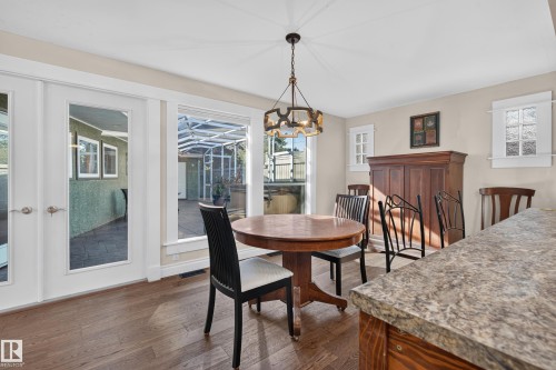 Wood-finish flooring, white French doors, expansive window, ceiling-mounted chandelier, and a stone-finish countertop - 11603 72 Avenue Nw, Edmonton, AB 