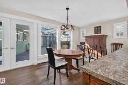 Wood-finish flooring, white French doors, expansive window, ceiling-mounted chandelier, and a stone-finish countertop - 