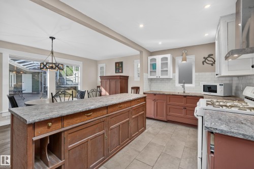 Kitchen featuring a large island with a stone-finish countertop, tile flooring, white subway tile backsplash, and stainless steel range hood - 11603 72 Avenue Nw, Edmonton, AB 