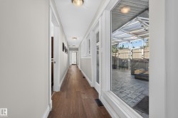 Wood-finish flooring throughout, featuring a long hallway with white trim, recessed lighting, and windows overlooking a covered outdoor patio with stamped concrete - 