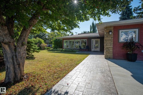 Landscaped front yard with mature trees, stamped concrete walkway, stone facade accents, and a double-door entry - 11603 72 Avenue Nw, Edmonton, AB 