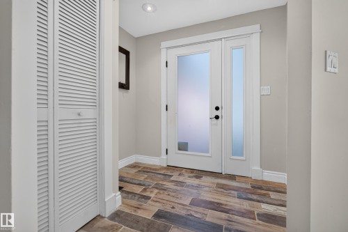 Entryway featuring wood-finish flooring, a white front door with frosted glass, a coordinating frosted glass sidelight, and white louvered bifold closet doors - 11603 72 Avenue Nw, Edmonton, AB 