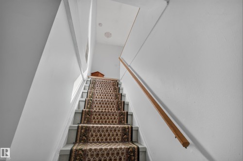 Staircase with a patterned runner, hardwood handrail, and overhead lighting - 11603 72 Avenue Nw, Edmonton, AB 