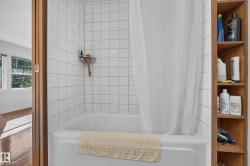 Bathtub with white tile surround, built-in wood shelving, and wood-paneled door frame - 