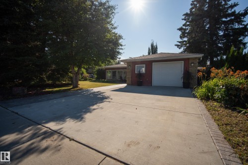 Concrete driveway with brick edging, attached garage with white door, red siding, stone accents, and established landscaping - 11603 72 Avenue Nw, Edmonton, AB 