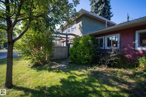 Stucco exterior with multiple window openings, surrounded by mature landscaping and a wooden fence - 11603 72 Avenue Nw, Edmonton, AB 