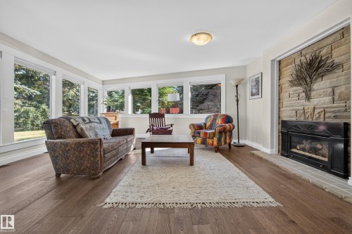 Wood-finish flooring, stone-clad fireplace with a black insert, white baseboards, and multiple large windows - 11603 72 Avenue Nw, Edmonton, AB 