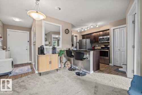 Kitchen featuring dark wood cabinetry, stainless steel appliances, and a breakfast bar with a dark countertop - #120 5370 Chappelle Rd Sw, Edmonton, AB 