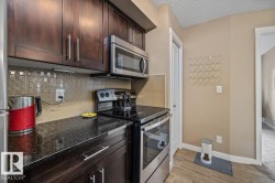 Kitchen featuring dark wood-finish cabinetry, stainless steel appliances, a tile backsplash, and dark countertops - 