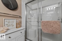 White paneled vanity with chrome hardware, full glass shower enclosure, and white tiled shower surround - 