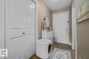 Wood-finish flooring, white paneled bifold doors, and a solid entry door with brushed nickel hardware - #120 5370 Chappelle Rd Sw, Edmonton, AB 