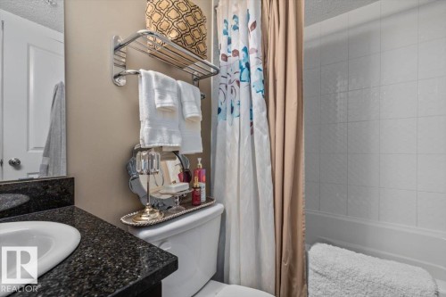 Bathroom featuring a built-in tub with tile surround, a vanity with a dark speckled countertop, an undermount sink, and a wall-mounted towel rack - #120 5370 Chappelle Rd Sw, Edmonton, AB 