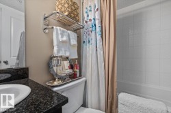 Bathroom featuring a built-in tub with tile surround, a vanity with a dark speckled countertop, an undermount sink, and a wall-mounted towel rack - 