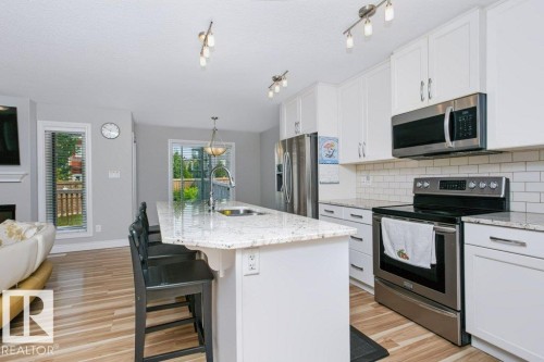 Modern kitchen featuring white cabinetry, stone countertops, stainless steel appliances, a subway tile backsplash, and wood-finish flooring - 3496 Weidle Way Sw, Edmonton, AB - Indoor Photo Showing Kitchen With Upgraded Kitchen