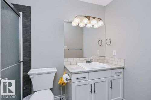 Bathroom featuring a frosted glass shower enclosure, dark tile shower surround, and a vanity with a white rectangular sink, light-toned countertop, and white subway tile backsplash - 3496 Weidle Way Sw, Edmonton, AB - Indoor Photo Showing Bathroom