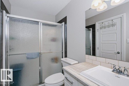 Bathroom featuring a shower with frosted glass enclosure, white subway tile backsplash, light-toned countertop, and a vanity with white cabinetry - 3496 Weidle Way Sw, Edmonton, AB - Indoor Photo Showing Bathroom