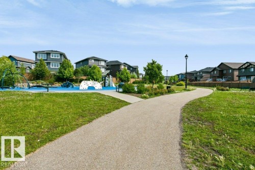 Expansive green space featuring a paved walking path, mature trees, and a children's play area with climbing structures and soft surfacing - 3496 Weidle Way Sw, Edmonton, AB - Outdoor
