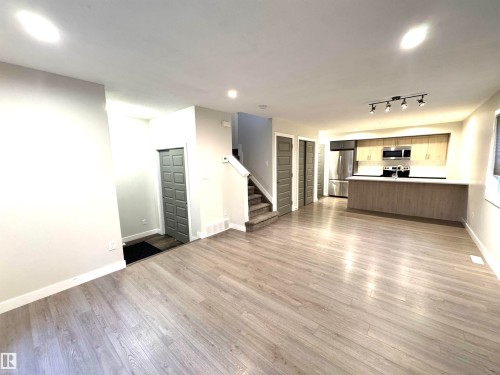 Light wood-finish flooring throughout, L-shaped kitchen island, stainless steel appliances, track lighting, and recessed ceiling lights - 12046 89 Street Nw, Edmonton, AB 