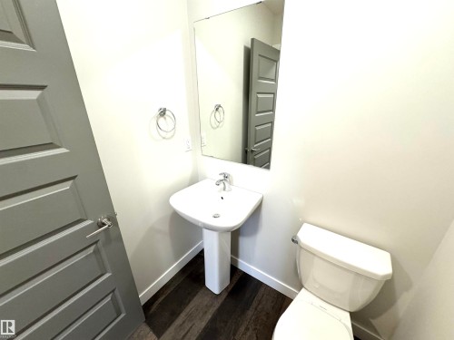 Pedestal sink, wall-mounted mirror, white toilet, wood-finish flooring, and a paneled door - 12046 89 Street Nw, Edmonton, AB 