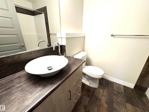 Vessel sink with chrome faucet, wood-finish vanity, toilet, full wall mirror, and wood-finish flooring - 12046 89 Street Nw, Edmonton, AB 
