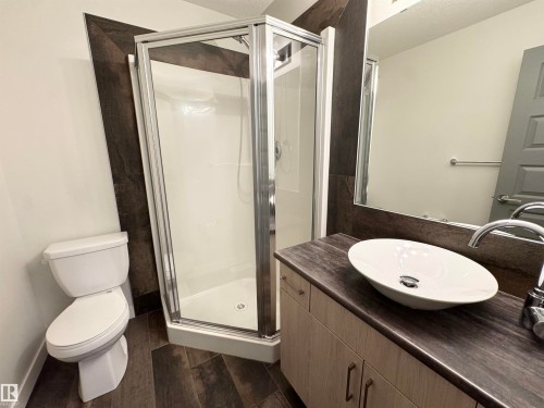 Walk-in shower with clear glass enclosure, modern vanity with wood-finish cabinetry, countertop with integrated vessel sink, and wood-finish flooring - 12046 89 Street Nw, Edmonton, AB 