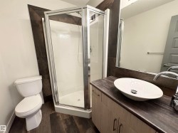 Walk-in shower with clear glass enclosure, modern vanity with wood-finish cabinetry, countertop with integrated vessel sink, and wood-finish flooring - 