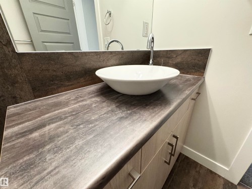 Modern vanity featuring a vessel sink, chrome faucet, wood-finish cabinetry, and a textured countertop - 12046 89 Street Nw, Edmonton, AB 