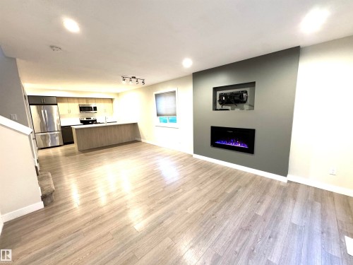 Open-concept living area with wood-finish flooring, a contemporary built-in electric fireplace, recessed lighting, and a kitchen island with a sink - 12046 89 Street Nw, Edmonton, AB 