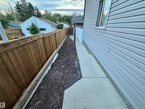 Siding exterior with a concrete walkway, wood-paneled fencing, and mulched landscaping - 12046 89 Street Nw, Edmonton, AB 