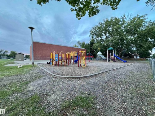 Brick exterior building with multiple playground structures, surrounded by mature trees and a gravel ground surface - 12046 89 Street Nw, Edmonton, AB 