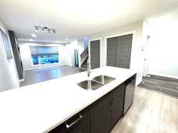 Open-concept living space featuring wood-finish flooring, a large window, a track lighting fixture, and a kitchen island with a double stainless steel sink - 
