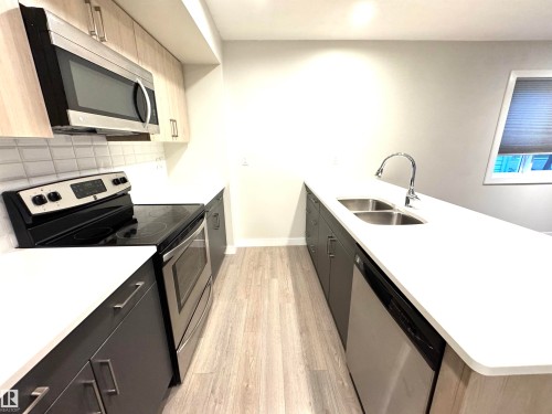 Contemporary kitchen featuring sleek cabinetry, light wood-finish flooring, white countertops, and stainless steel appliances - 12046 89 Street Nw, Edmonton, AB 