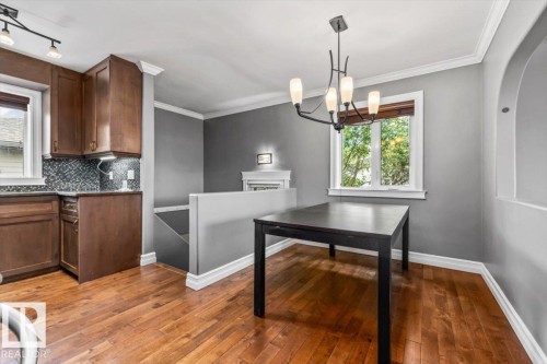Wood-finish flooring throughout, dark wood-finish cabinetry, patterned tile backsplash, white window trim, and a decorative arched wall feature - 10994 165 Street Nw, Edmonton, AB 