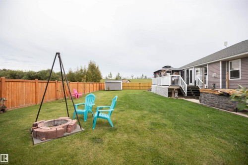 Expansive backyard featuring a manicured lawn, wood privacy fence, and a built-in fire pit - 6003 50 Ave, Barrhead, AB 