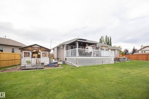 Expansive backyard with a large deck featuring white railings, a covered seating area, and a separate outbuilding with multiple windows - 6003 50 Ave, Barrhead, AB 