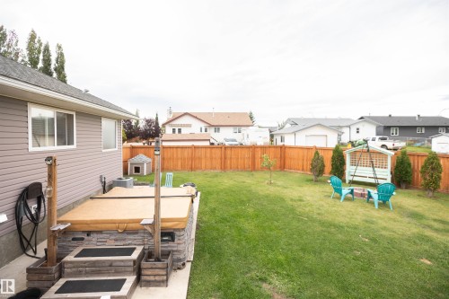 Expansive backyard featuring a stone-clad hot tub with wooden steps, a durable wood fence, and mature landscaping - 6003 50 Ave, Barrhead, AB 