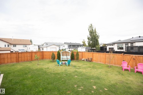 Expansive backyard with a manicured lawn, complete wood fence perimeter, and mature landscaping - 6003 50 Ave, Barrhead, AB 