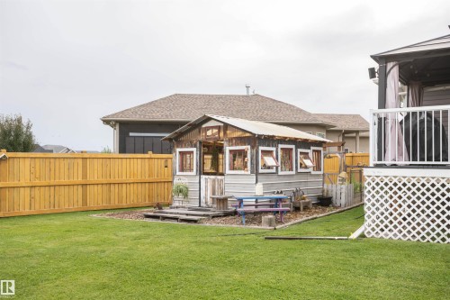 Expansive backyard featuring a manicured lawn, a wooden fence, and a gazebo with white railing - 6003 50 Ave, Barrhead, AB 